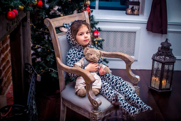 Jolie petite fille souriante avec un ours en peluche près du sapin de Noël assis sur une chaise vintage. Bonne année . — Photo