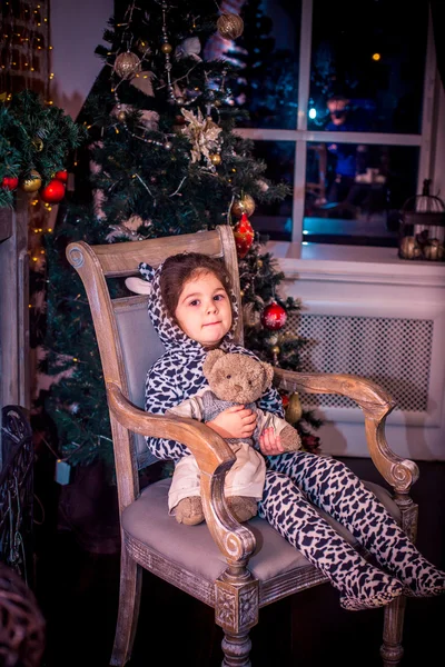 Jolie petite fille souriante avec un ours en peluche près du sapin de Noël assis sur une chaise vintage. Bonne année . — Photo