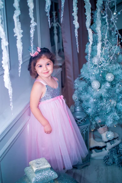 Kis lány öltözött szép divat fehér virág ruha pózol a karácsonyfa közelében — Stock Fotó