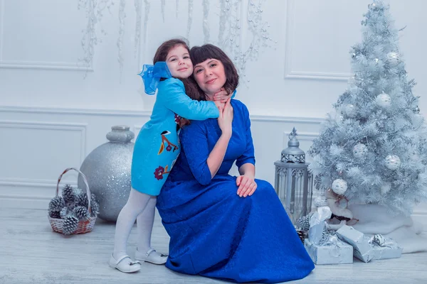 Ευτυχισμένη μητέρα με την κόρη της στο μακρύ μπλε φορέματα δασοσυστάδα κοντά το χριστουγεννιάτικο δέντρο — Φωτογραφία Αρχείου