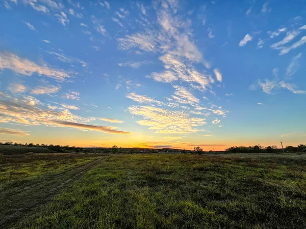 Çimenli kırsal alan renkli bir günbatımı gökyüzünün altında toprak bir yol gösteriyor