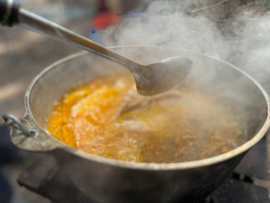 Geleneksel sıcak güveci, açık havada buharlı bir kazanda kepçeyle karıştırmak