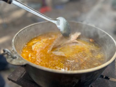 Kepçeli dökme demir bir kazanda kaynayan balık çorbası.