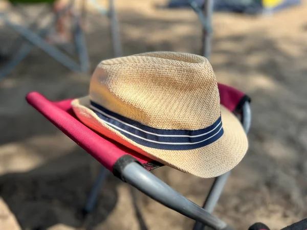 Mavi bantlı hasır şapka plajda kırmızı bir kamp sandalyesinde dinleniyor.