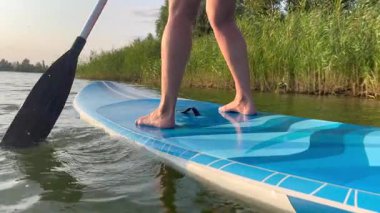 Gün batımında sakin suda süzülen bir insanın ayakta duran ayaklarının yakın çekimi.