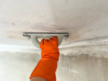 Turuncu eldiven takan işçiler tavan alçısını bir aletle zımparalıyorlar.