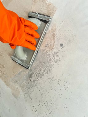 Turuncu eldiveni boyamak için hazırlanmış duvarı zımparalıyor.