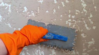 Profesyonel sıvacılar duvara dekoratif alçı uygulamak için bir kürekle eldiven giyerler.