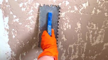 Turuncu eldivenli inşaat işçisi duvara dekoratif alçı uygulamak için çentik mala kullanıyor.