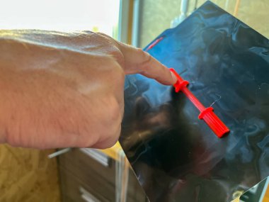 İnsan parmağı, siyah yansıtıcı yüzeyde duran kırmızı plastik bir nesneyi işaret ediyor.