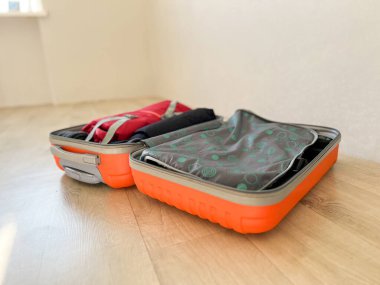 Turuncu bavul ahşap bir zeminde, içinde giysiler ve bir yolculuğa hazırlanıyor.