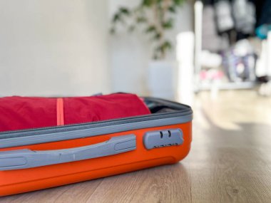 Turuncu bavul yerde, tatil için kırmızı giysileri topluyor.