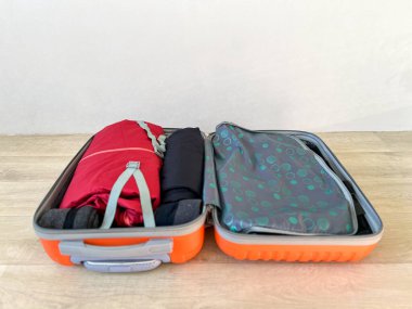 Ahşap zeminde paketlenmiş giysileri gösteren bavulu aç