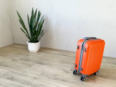 Turuncu bavul, tahta zemindeki yılan fabrikasının yanında duruyor. Seyahat ve tatili temsil ediyor.