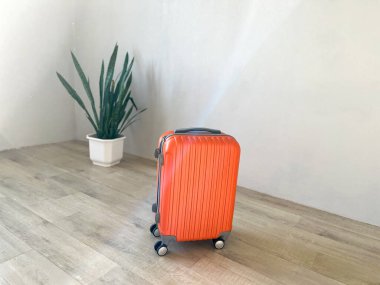 Parlak turuncu bir bavul, minimalist bir odada, açık ahşap bir zeminde duruyor.