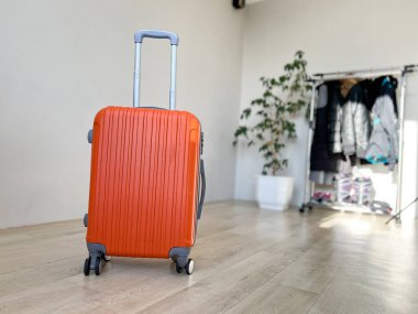 Tekerlekli parlak turuncu bavul, geniş saplı, yolculuk için hazırlanmış.