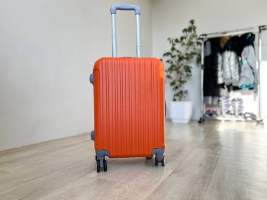 Geniş saplı turuncu bavul ve tekerlekler parlak bir iç mekanda yolculuğa hazır.