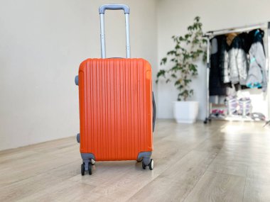 Turuncu valiz ahşap zeminde duruyor, yolculuk için hazırlanıyor.