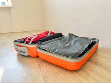 Tahta bir zeminde seyahat için giysi ve gerekli eşyalarla dolu açık bir bavul.