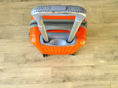 Parlak turuncu bavul, parke zeminde bekliyor, yolculuk için hazır.