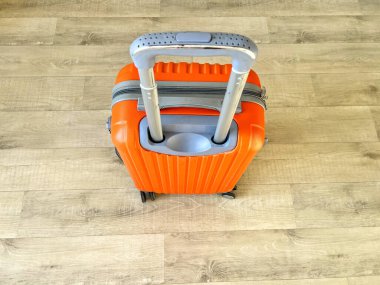 Parlak turuncu bavul, açık ahşap bir zeminde dimdik duruyor.