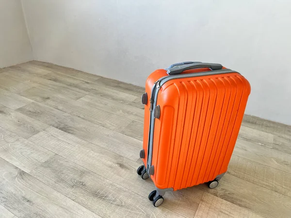 Turuncu bavul tatile hazır. Boş odadaki açık tahta zeminde.