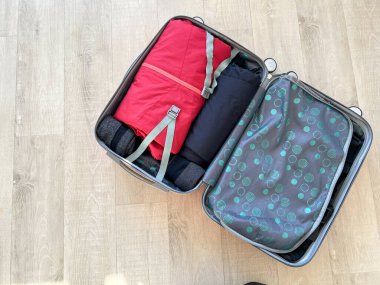 Ahşap bir zeminde içi giysi dolu bavulu aç, yolculuğa hazır.