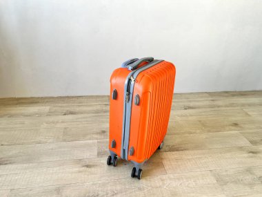 Turuncu bavul, hafif ahşap bir zeminde dimdik duruyor, yolculuğa hazır.