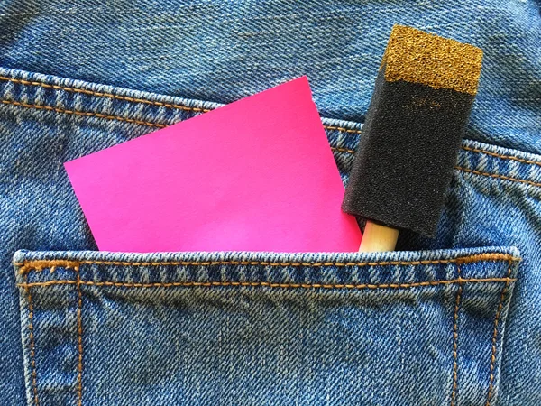 蓝色斜纹棉布牛仔裤口袋里有泡沫涂料刷的粉红色粘贴字条 — 图库照片