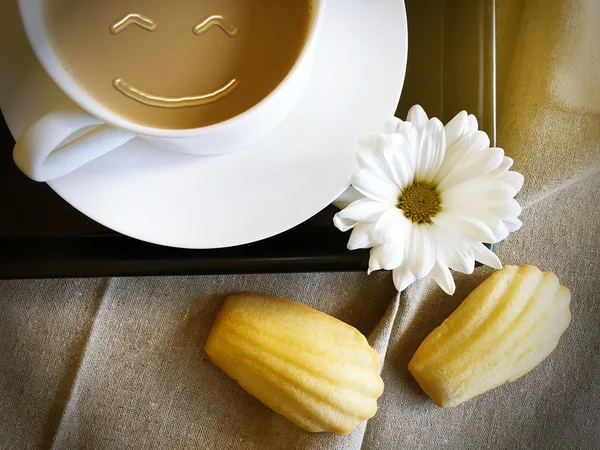 Французские мадлен с кофе и белой маргариткой и улыбающимся лицом — стоковое фото