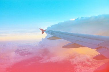 Bir uçağın kanadı, akşam üstü bulutların üzerinde pembe ve mavi gökyüzünde.