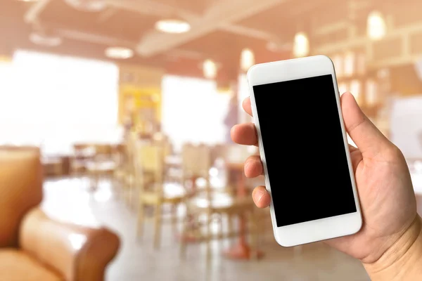 Woman hand holding smartphone against blur bokeh of coffee shop — Stock Photo, Image