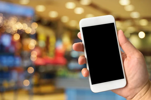 Woman hand holding smartphone against blur bokeh of shop backgro — Stock Photo, Image