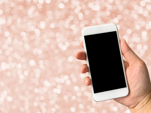 Woman hand holding smartphone against rose gold bokeh abstract b — Stock Photo, Image