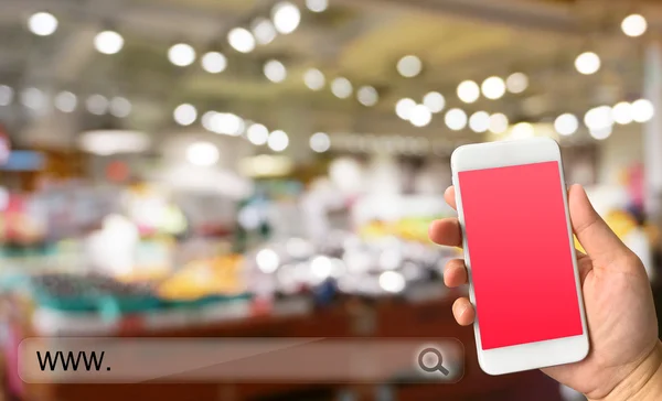 Woman hand holding smartphone against blur bokeh ofstore backgro — Stock Photo, Image