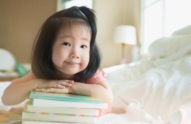 Asyalı bebek portresinin resmi, gururla kitap yığınını sunarken, küçük kitap kurtları akıllı çocuk olmayı öğrenirken, okul öncesi çocuklar için sevimli çocuk kitapları okurken..