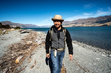 Sırt çantalı Asyalı bir adamın portresi. Kameraya gülümsüyor. Wanaka Gölü 'nün yanındaki kaldırımda yürürken..