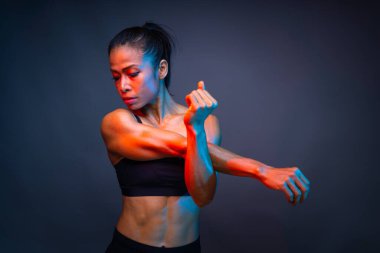 Altı çekirdekli kaslı sağlıklı bir Asyalı kadının üst vücut parçası koyu arkaplan eğitimi sırasında kas hasarını azaltmak için spor yapmadan önce sağ ve sol kolunu esnetiyor..