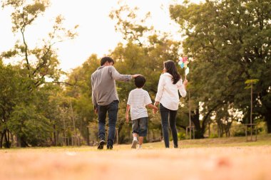 Asyalı mutlu ailenin arkasından gelen sahne, sonbaharda öğleden sonra parkta yürüyüş ve rahatlama konsepti aile birliği, sıcak kalpli aile, ebeveynlik, mutlu aile gezisi..