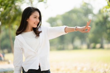 Kendine güvenen, gülümseyen ve iki parmağını kaldıran muhteşem Asyalı kadının yan görünüşü, arka planda zafer işareti, kendine güvenen kadın kavramı, mutlu ve uysal kadın gücü..