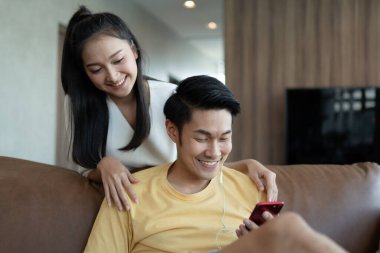 Akıllı telefonu güzel bir kadının arkasında müzik dinlemek için kullanan bir adam oturma odasında çekici bir Asyalı çift mutlu genç adam ve kadın sıradan bir yaşam tarzında. Sevgili karı koca ilişkisi..
