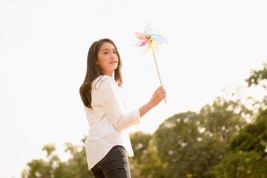 Güzel Asyalı kadın elinde yel değirmeniyle parkta iyi vakit geçiriyor. Fotokopi alanı, tasasız kadın konsepti, mutlu yaşam tarzı, akıllı enerji tasarrufu, alternatif enerji, temiz çevre..