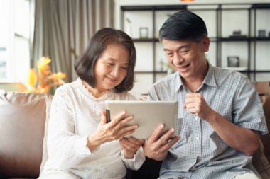 Sahnedeki yaşlı Asyalı çift, evde tek başına dolaşırken akıllı telefondan bir video konferans görüşmesi yapıyor..