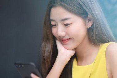 Genç Asyalı kadın cep telefonuna bakıyor ve gülümsüyor, ofis zamanındaki genç subay yaşam tarzı kavramı, sol taraftaki boşluğu kopyalıyor..