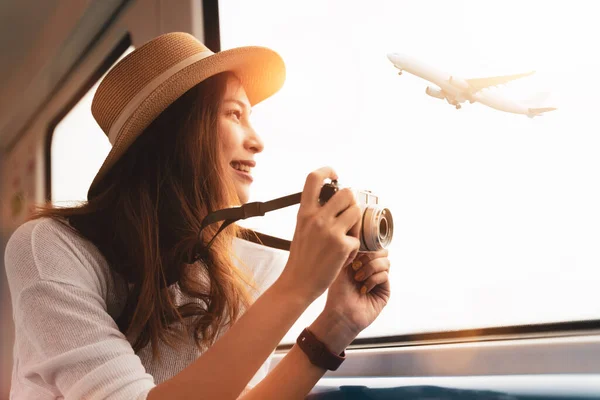 Scene of a young woman tourist smiling while holding the camera and looking up to the sky that have airplane flying. Adventure calling,  Girl explore the world. Big dream come through. Vacation trip.