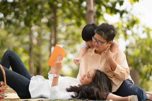 Happy Asian family mother son and granny enjoy picnic time at the park together, spending good time together having fruits and enjoy park atmosphere, family relaxed activity, casual weekend activity.