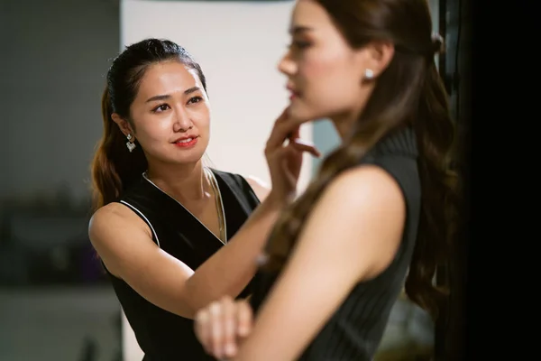 Selective focus of happy Asian makeup artist putting on more lipstick to the actress or model behind the scene, concept of pride of profession, professional occupation, skilled professional career.