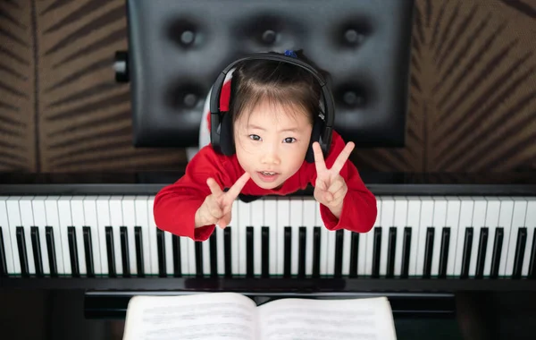 3 yaşındaki çocuk piyano, e-öğrenme, yeni normal, çevrimiçi öğrenme, müzik eğitimi, erken çocukluk, aktivite, üst bakış açısı çaldıktan sonra başını kaldır ve zafer işareti göster.