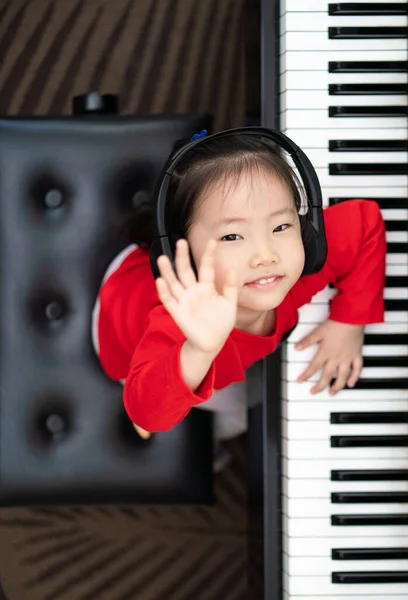 Küçük Asya 'lı kızın dikey görüntüsü küçük gülümsemeyle piyano çalarken, müzik aletlerini keşfederken, çevrimiçi öğrenirken, erken çocukluk müzik eğitimi, boş zaman aktiviteleri yaparken kameraya bakar..