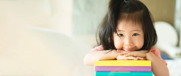 Asyalı bebek portresinin panoramik kitabı çenesini kaldırdı ve ellerini kitapların üzerine koydu, küçük kitap kurtlarının zeki çocuk olmayı öğrenmesi, anaokulu için sevimli çocuk kitabı okuması,.